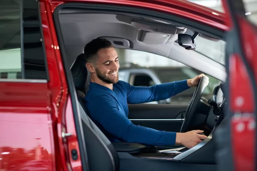 A young man sits in the front seat of the vehicle he purchased with a low credit auto loan.